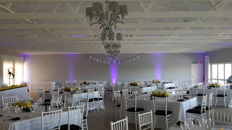 Wedding reception venue with white table settings and purple uplighting